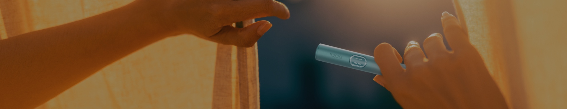 Hands holding a curtain and a IQOS ILUMA i Prime Holder in warm sunlight.